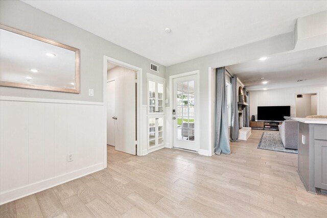 interior space featuring visible vents, light wood finished floors, wainscoting, and a fireplace