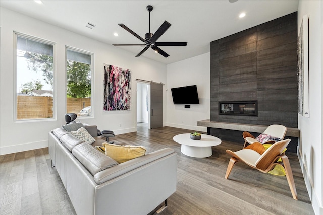 living room with ceiling fan, visible vents, wood finished floors, a barn door, and baseboards