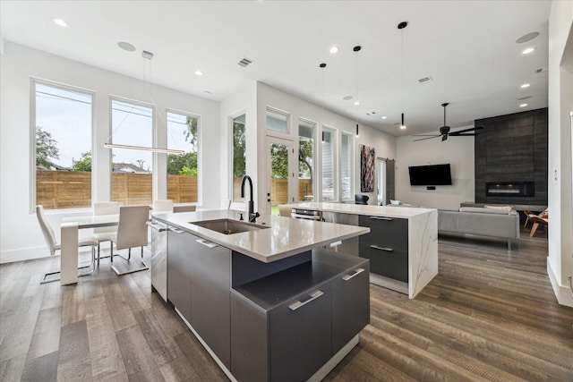 kitchen with a kitchen island with sink, modern cabinets, a sink, dark wood finished floors, and decorative light fixtures