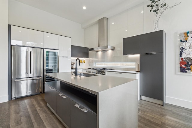 kitchen featuring high end fridge, modern cabinets, wall chimney range hood, dark wood-type flooring, and a sink