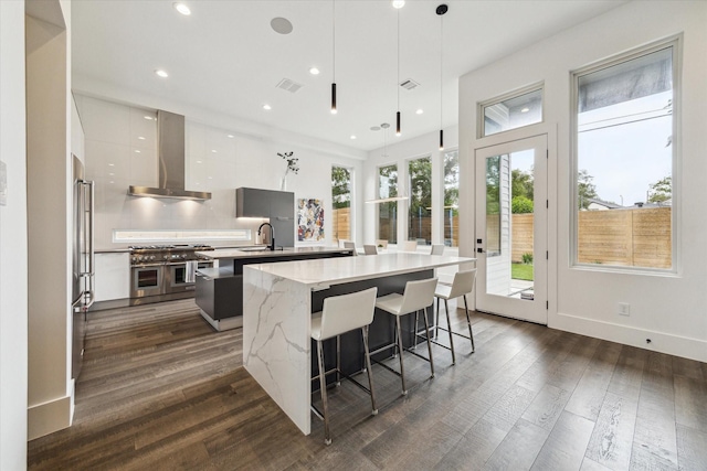 kitchen featuring wall chimney range hood, dark wood-style flooring, a center island, high end appliances, and modern cabinets