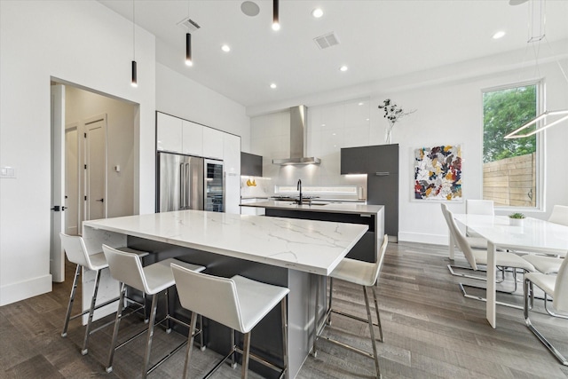 kitchen featuring wall chimney range hood, modern cabinets, white cabinetry, a spacious island, and high quality fridge