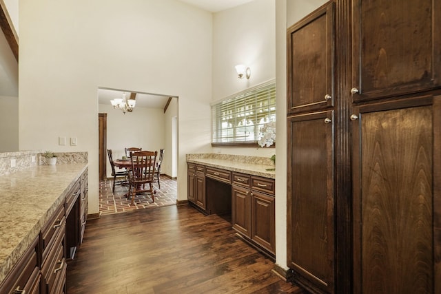 kitchen featuring dark brown cabinetry, a towering ceiling, light stone counters, a notable chandelier, and dark wood-type flooring