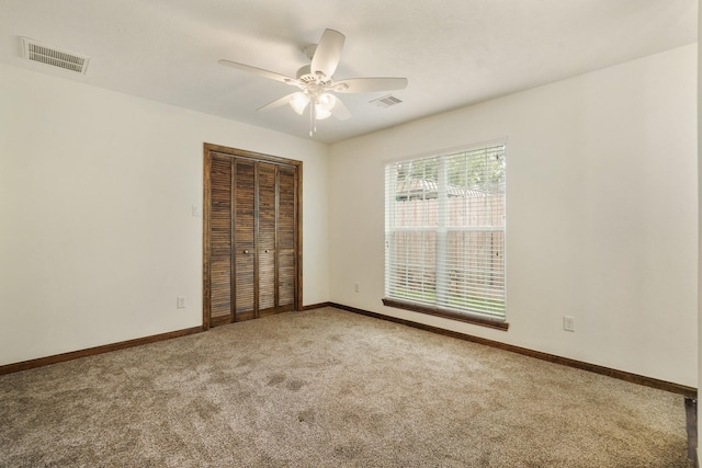 empty room with carpet floors, a ceiling fan, baseboards, and visible vents