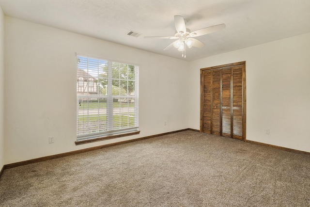 carpeted empty room with ceiling fan, visible vents, and baseboards