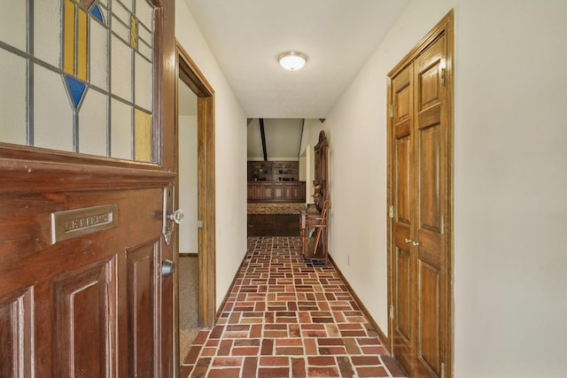 corridor with baseboards and brick floor