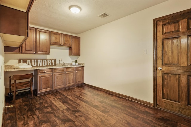kitchen featuring a sink, brown cabinetry, baseboards, visible vents, and dark wood-style floors