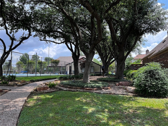 view of community with fence, a tennis court, and a lawn