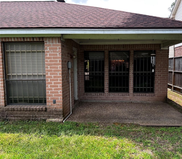 view of exterior entry featuring brick siding, fence, and a shingled roof