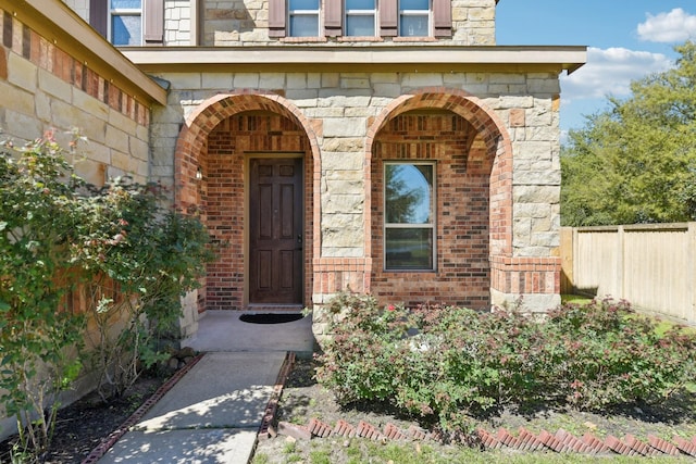 entrance to property featuring brick siding, fence, and stone siding