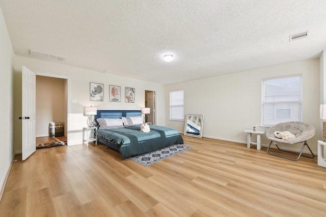 bedroom with visible vents, a textured ceiling, and light wood finished floors