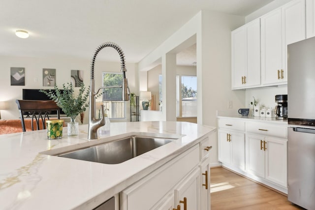 kitchen with freestanding refrigerator, white cabinets, a sink, and light wood-type flooring