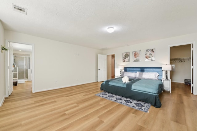 bedroom with visible vents, baseboards, a walk in closet, a textured ceiling, and light wood finished floors