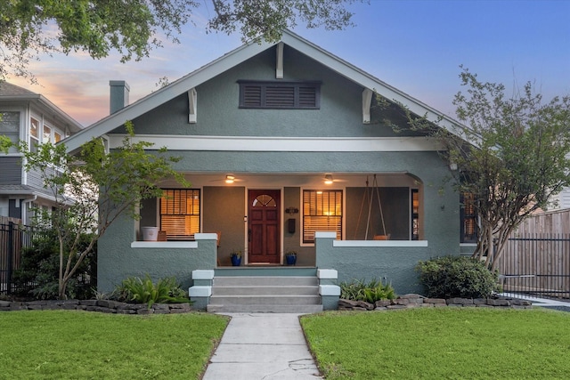 bungalow featuring a yard, fence, covered porch, and stucco siding