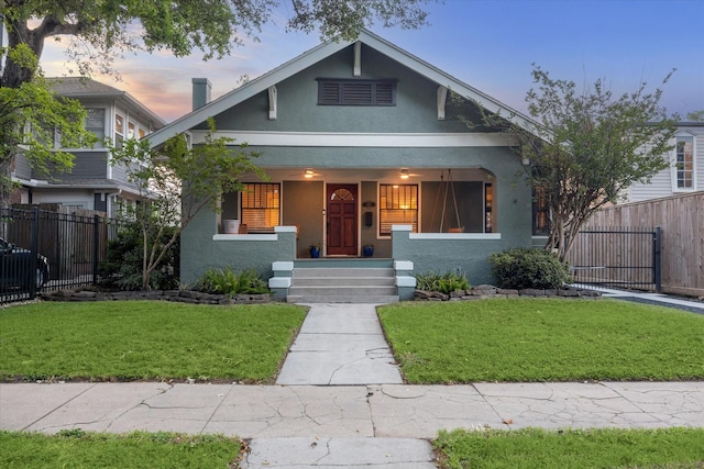 bungalow featuring a lawn, fence, covered porch, and stucco siding