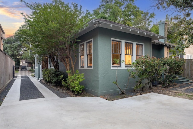property exterior at dusk with a chimney, a gate, fence, a patio, and stucco siding