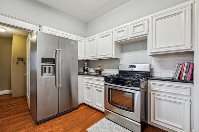 kitchen with dark wood-style flooring, dark countertops, appliances with stainless steel finishes, and tasteful backsplash