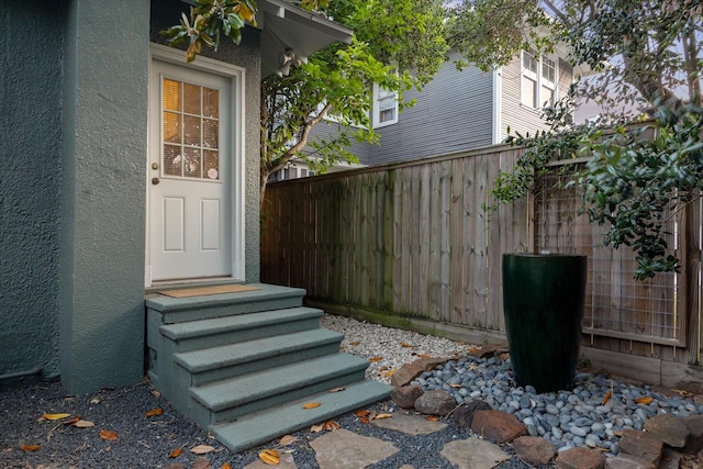 view of exterior entry with fence and stucco siding