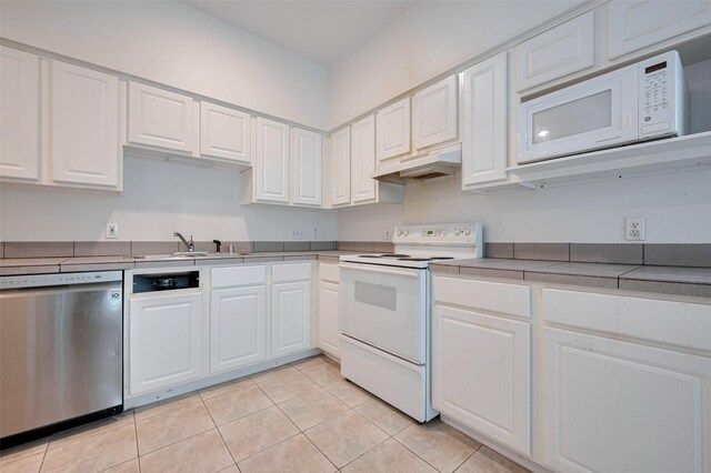kitchen with white appliances, white cabinets, under cabinet range hood, and a sink