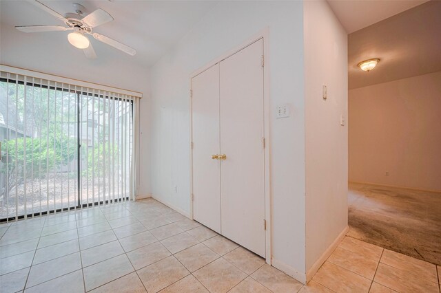empty room featuring light tile patterned flooring, light colored carpet, a ceiling fan, baseboards, and vaulted ceiling