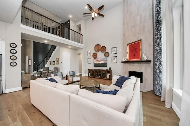 living room featuring a ceiling fan, a towering ceiling, wood finished floors, and a fireplace