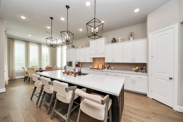 kitchen with decorative backsplash, a center island with sink, a sink, an inviting chandelier, and stainless steel appliances