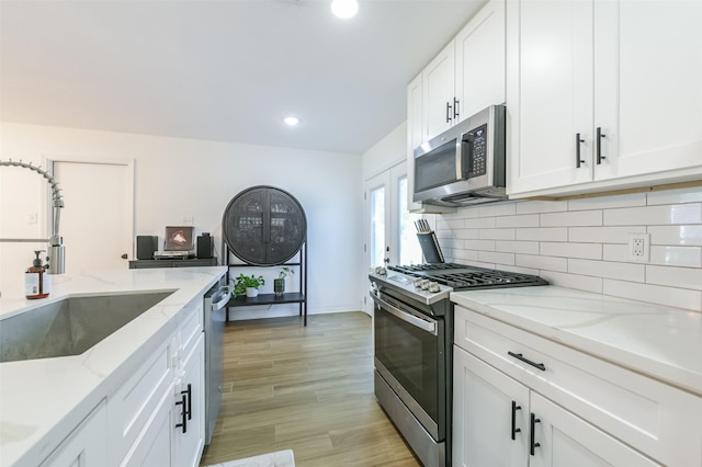 4110 Lou Anne Ln, Houston, TX 77092 - kitchen with stainless steel appliances, a sink, backsplash, white cabinets, and light wood-style floors