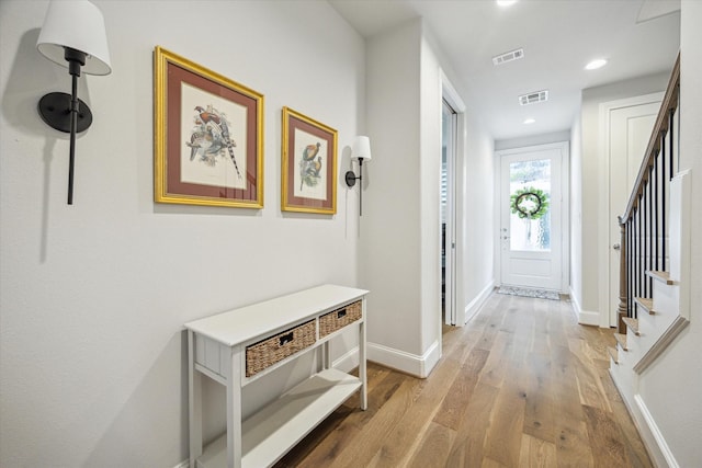 hallway featuring visible vents, baseboards, wood finished floors, and stairway