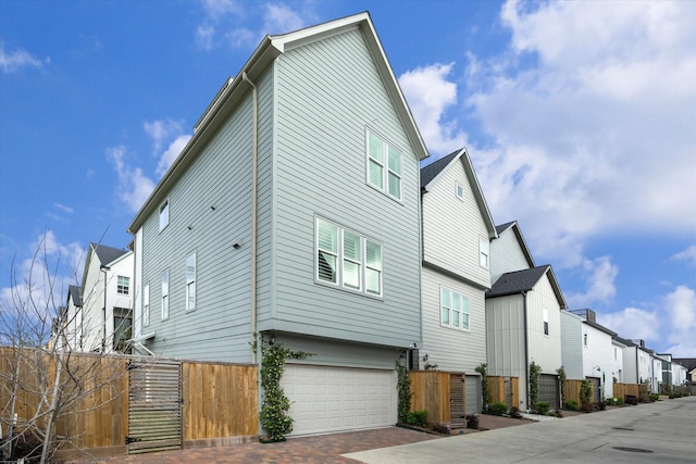view of side of home with a garage, decorative driveway, fence, and a residential view
