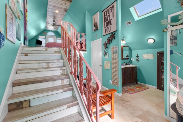 stairs featuring ceiling fan, visible vents, baseboards, tile patterned floors, and lofted ceiling with skylight