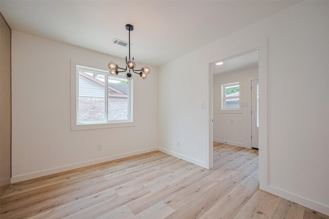 spare room featuring baseboards, light wood-type flooring, a chandelier, and visible vents