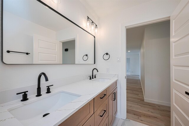 full bath featuring double vanity, a sink, baseboards, and wood finished floors