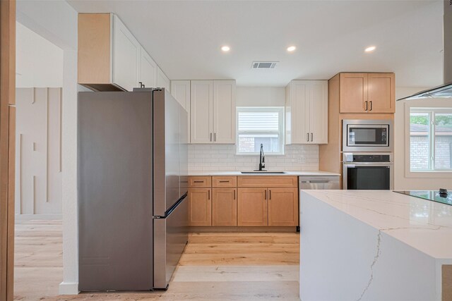 kitchen featuring visible vents, a sink, light wood finished floors, appliances with stainless steel finishes, and backsplash