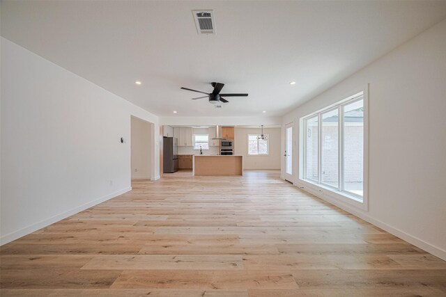 unfurnished living room with visible vents, baseboards, recessed lighting, light wood-type flooring, and ceiling fan with notable chandelier