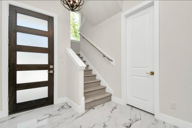 foyer entrance with stairs, baseboards, an inviting chandelier, and marble finish floor