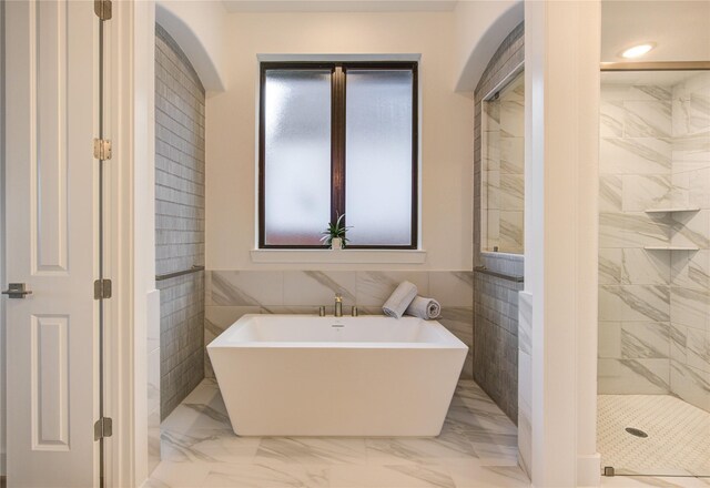 full bath with marble finish floor, a freestanding bath, tile walls, and a shower stall
