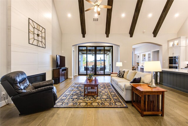 living area featuring visible vents, a ceiling fan, light wood-style floors, high vaulted ceiling, and arched walkways
