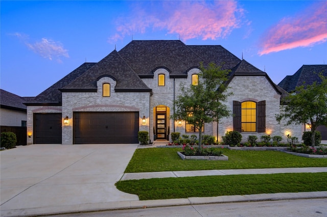 french country home featuring a yard, brick siding, an attached garage, and concrete driveway