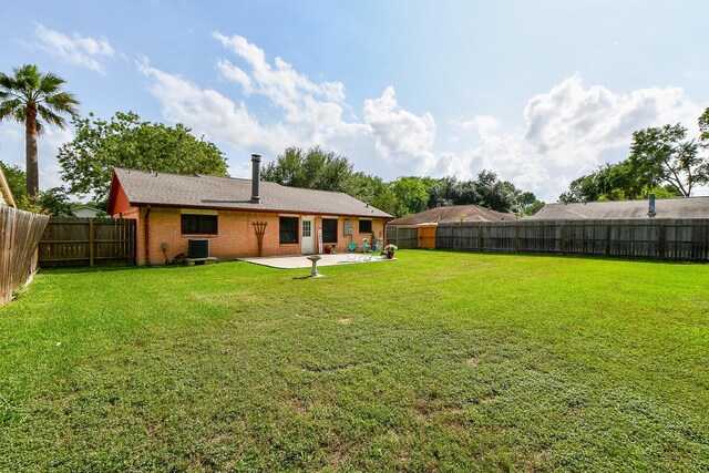 back of property with a yard, brick siding, a fenced backyard, and a patio area