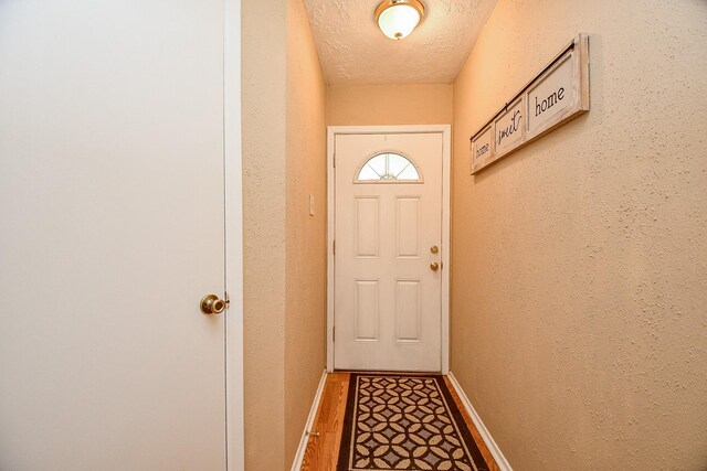 doorway with baseboards, a textured ceiling, and wood finished floors