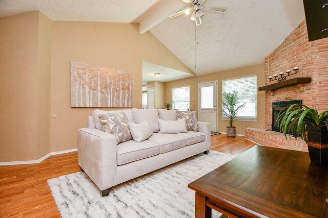 living area featuring a fireplace, baseboards, lofted ceiling with beams, a ceiling fan, and light wood-style flooring