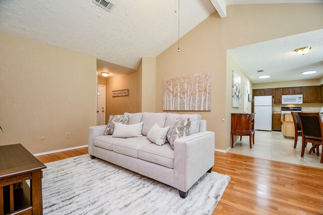 living area with visible vents, baseboards, vaulted ceiling with beams, a textured ceiling, and light wood finished floors