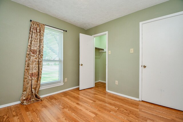 unfurnished bedroom featuring light wood-type flooring, a textured ceiling, baseboards, and a walk in closet