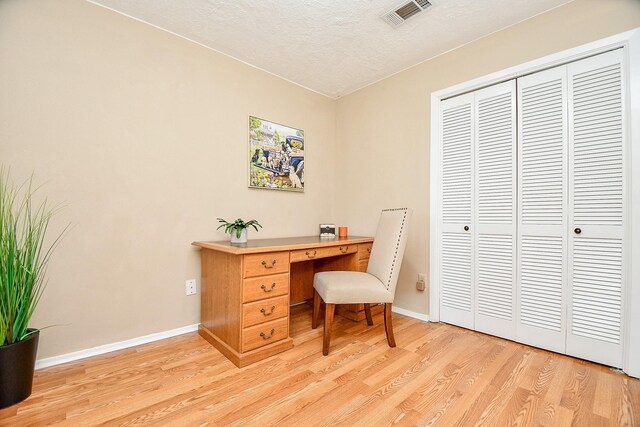 office with a textured ceiling, baseboards, visible vents, and light wood finished floors