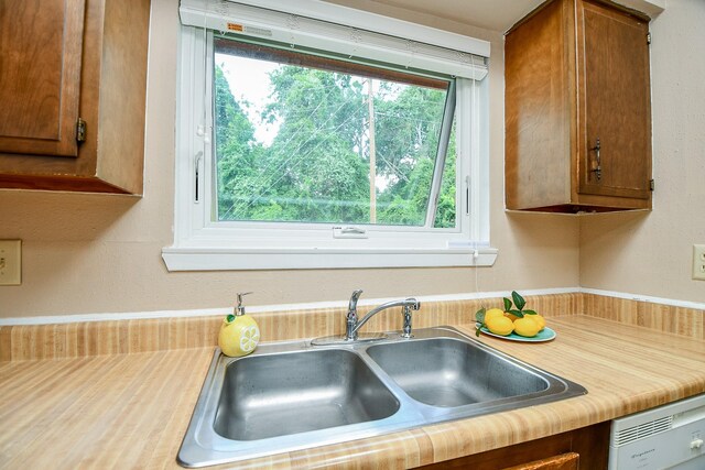 kitchen featuring brown cabinetry, a sink, dishwashing machine, and light countertops