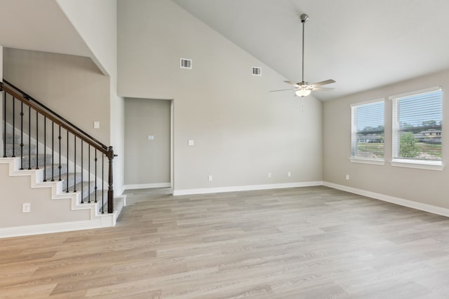 unfurnished room featuring high vaulted ceiling, light wood-style flooring, stairs, a ceiling fan, and baseboards