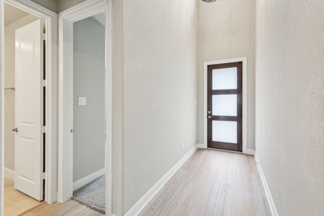 hall featuring baseboards, a textured wall, and light wood finished floors