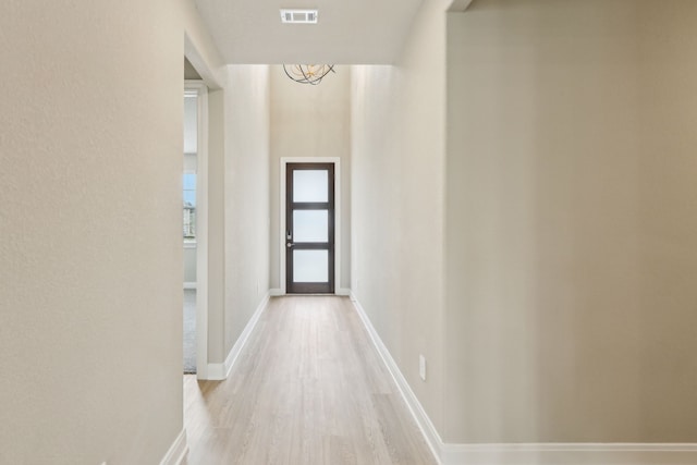 hallway with baseboards, a notable chandelier, visible vents, and light wood-style flooring