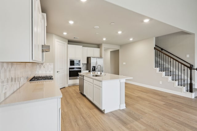 kitchen featuring white cabinets, appliances with stainless steel finishes, a sink, light wood-style flooring, and recessed lighting