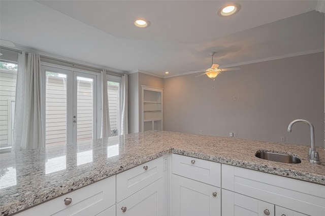 kitchen with a sink, light stone counters, a ceiling fan, and a healthy amount of sunlight